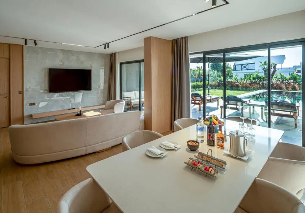 Großer Wohnraum mit gedecktem Esstisch, Sofa, Fernseher und Schiebetüren zur Sonnenterrasse.