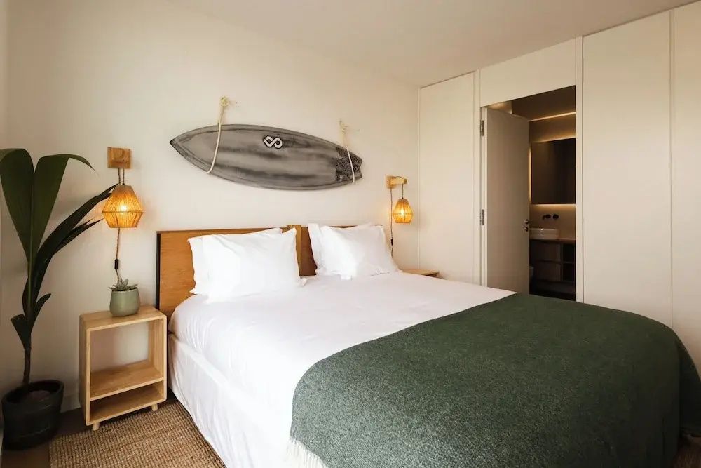 Doppelbett mit weißer Bettwäsche, grüner Tagesdecke und einem dekorativen Surfbrett über dem Kopfteil.