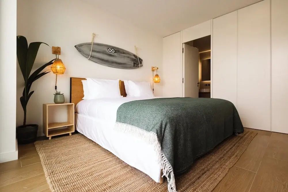 Helles Doppelzimmer mit Holzmöbeln, geflochtenem Teppich und Sichtachse ins angrenzende Badezimmer.