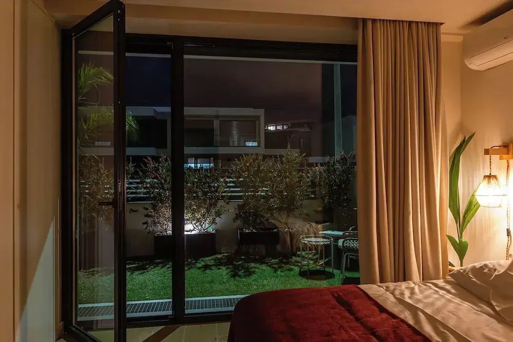 Blick durch die geöffnete Terrassentür auf eine beleuchtete Terrasse mit Pflanzen am Abend.