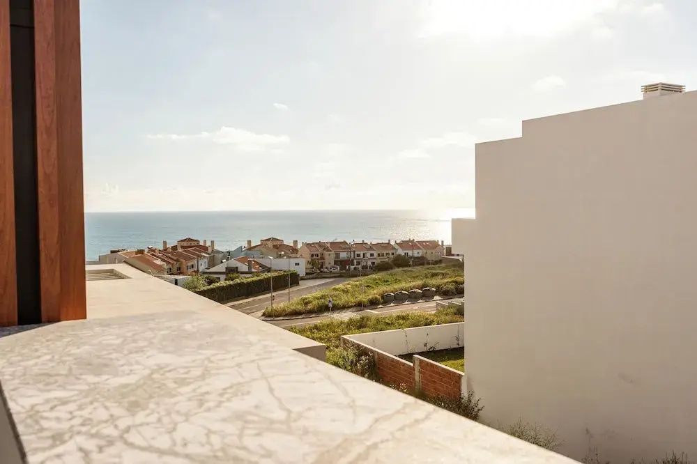 Blick von der Terrasse über Häuserdächer auf das blaue Meer unter sonnigem Himmel.