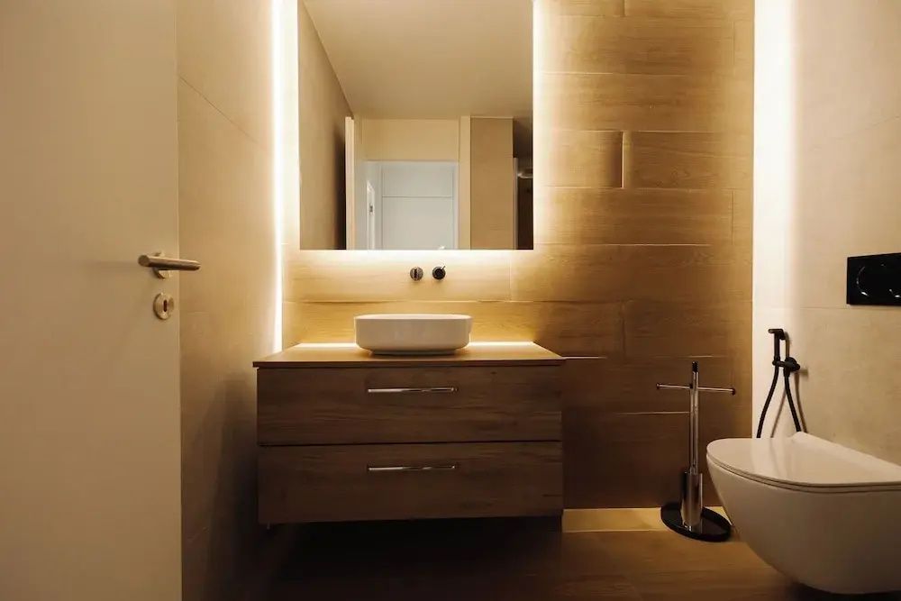 Modernes Badezimmer mit Holzwaschtisch, Aufsatzwaschbecken und beleuchtetem Spiegel.
