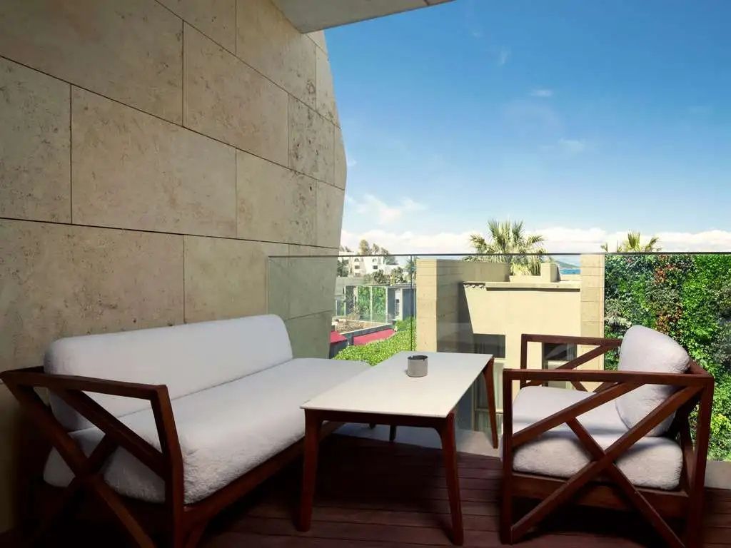 Überdachter Balkon mit weißem Sofa, Holzstühlen, Tisch und Ausblick ins Grüne.