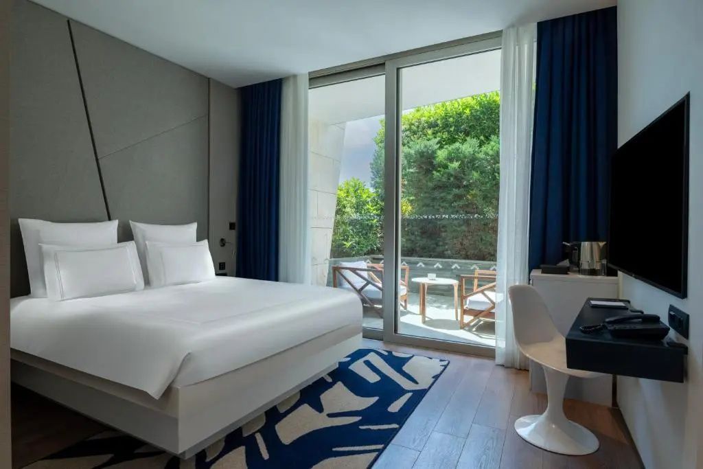 Modernes Hotelzimmer mit Doppelbett, Parkettboden und Blick auf den Balkon.
