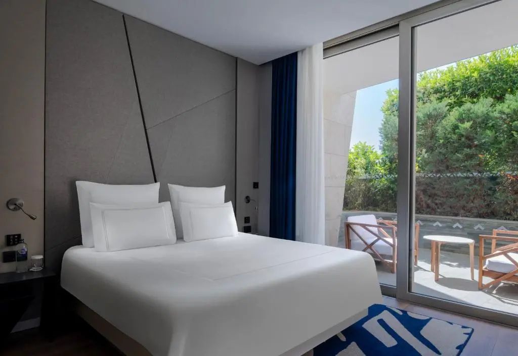 Doppelbett in hellem Hotelzimmer mit grauer Wandgestaltung und Terrasse.