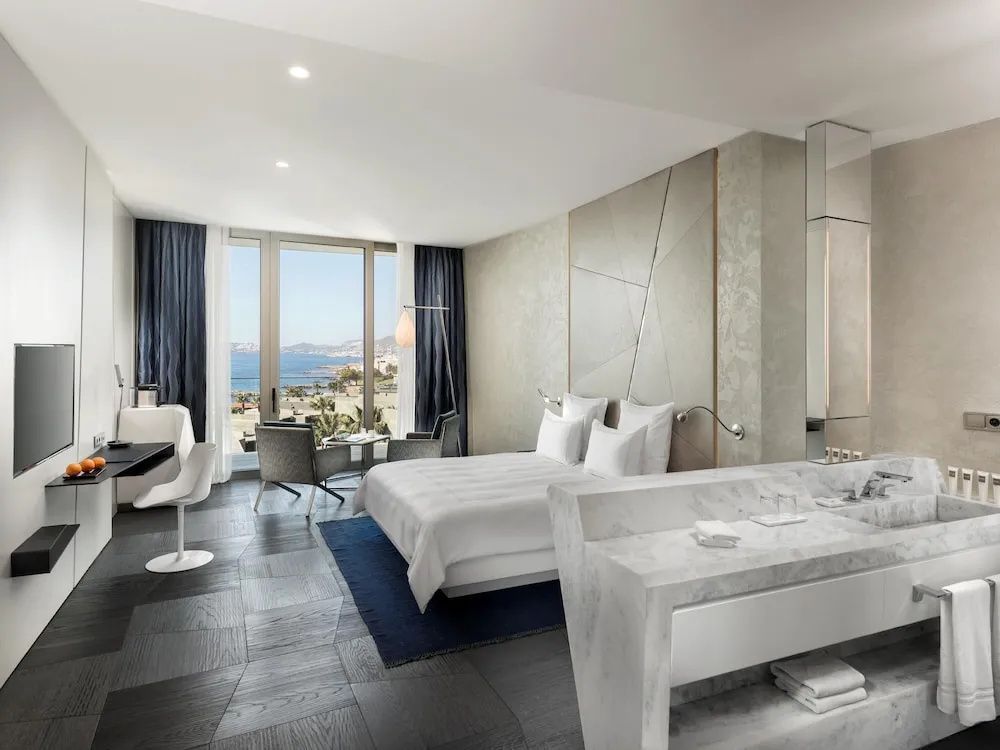 Modernes Hotelzimmer mit Doppelbett, Marmorelementen und Meeresblick durch große Fenster.