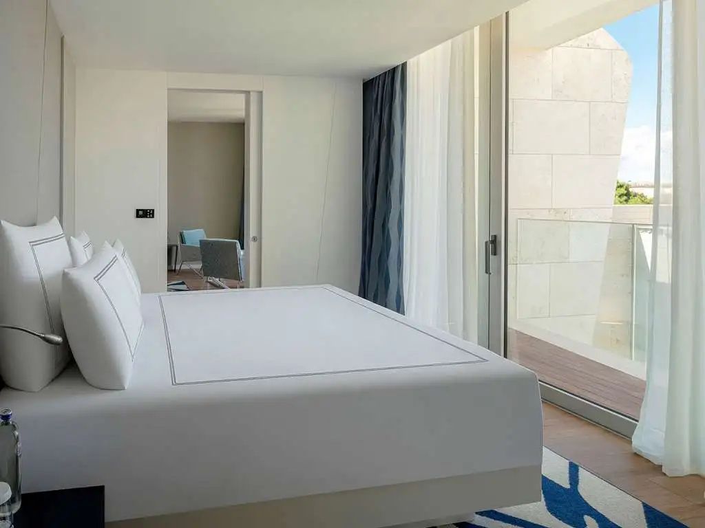 Modernes Hotelzimmer mit großem Doppelbett, weißer Bettwäsche und Zugang zum Balkon.