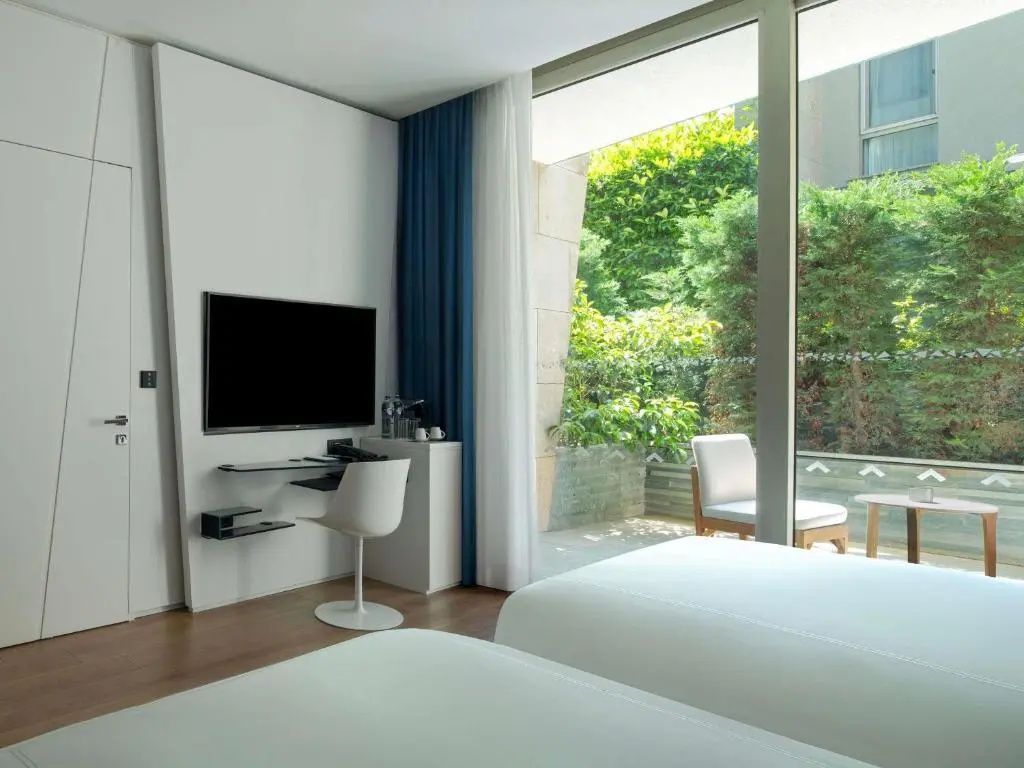 Schreibtischbereich mit Fernseher und Stuhl im Hotelzimmer vor Fenster.