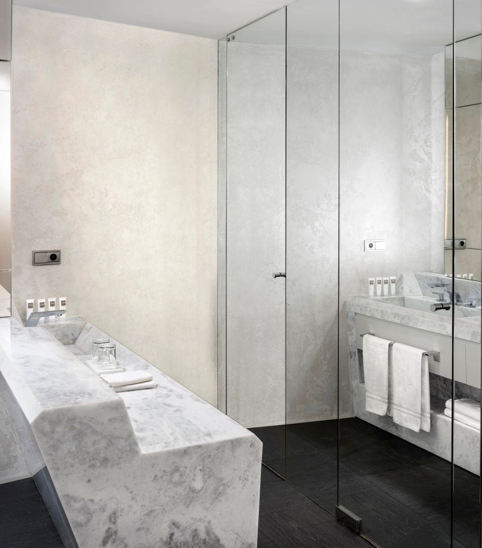 Badezimmer mit zwei Waschtischen aus hellem Marmor und Dusche hinter Glas.