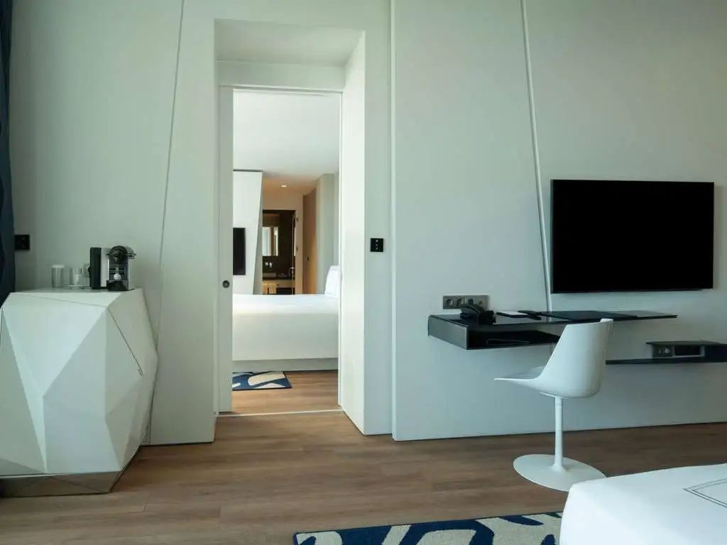 Wohnbereich eines Hotelzimmers mit Schreibtischecke und Blick in das Schlafzimmer.