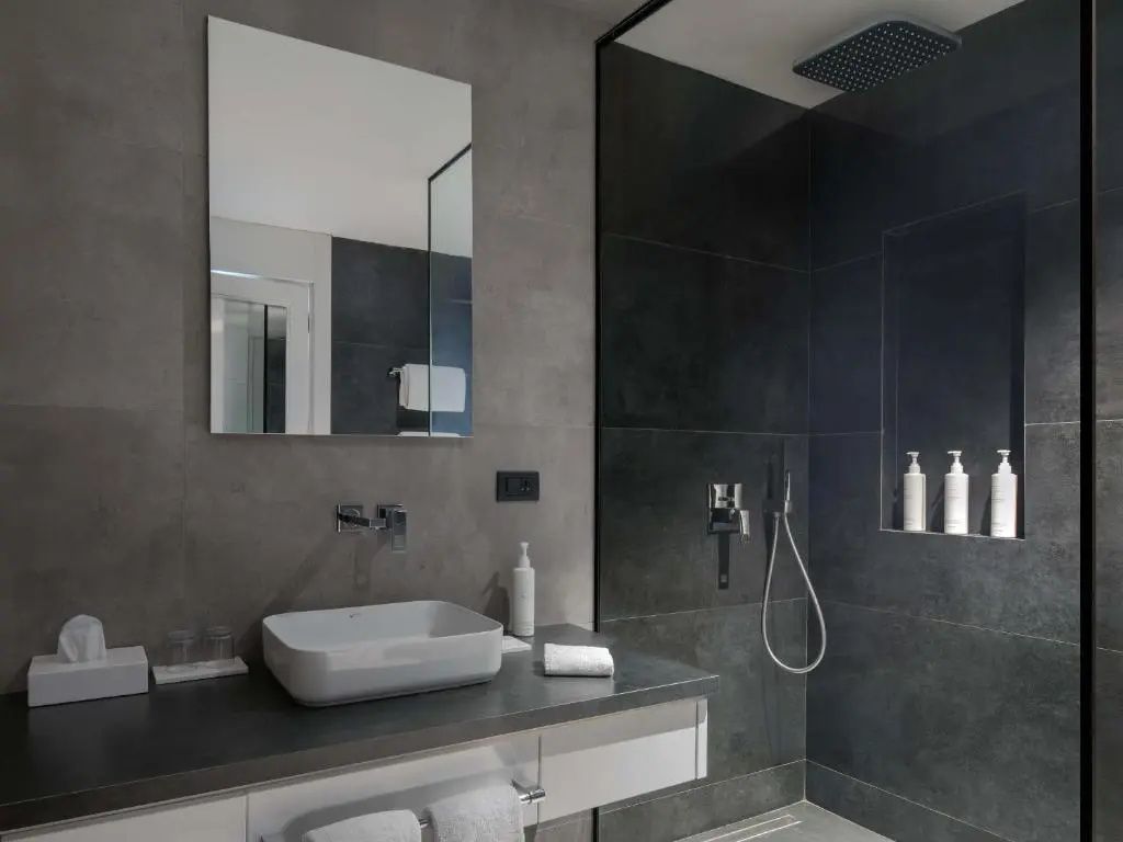 Badezimmer mit dunklen Fliesen, Regendusche und modernem Waschtisch.