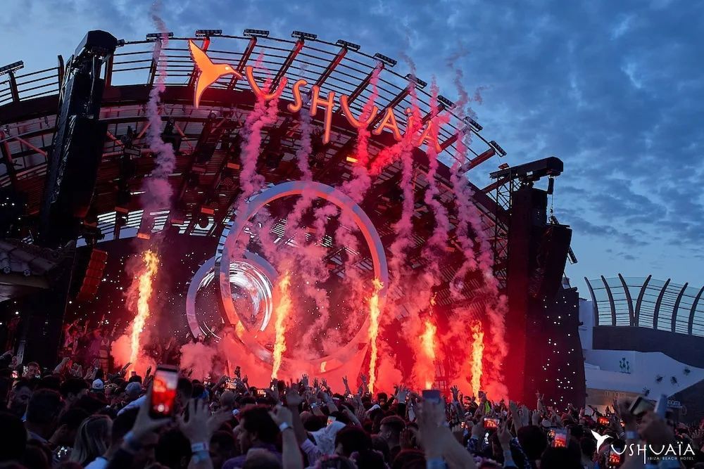 Bühnenaufbau von Ushuaïa mit Feuersäulen, Rauch und zahlreichen Menschen am Abend.
