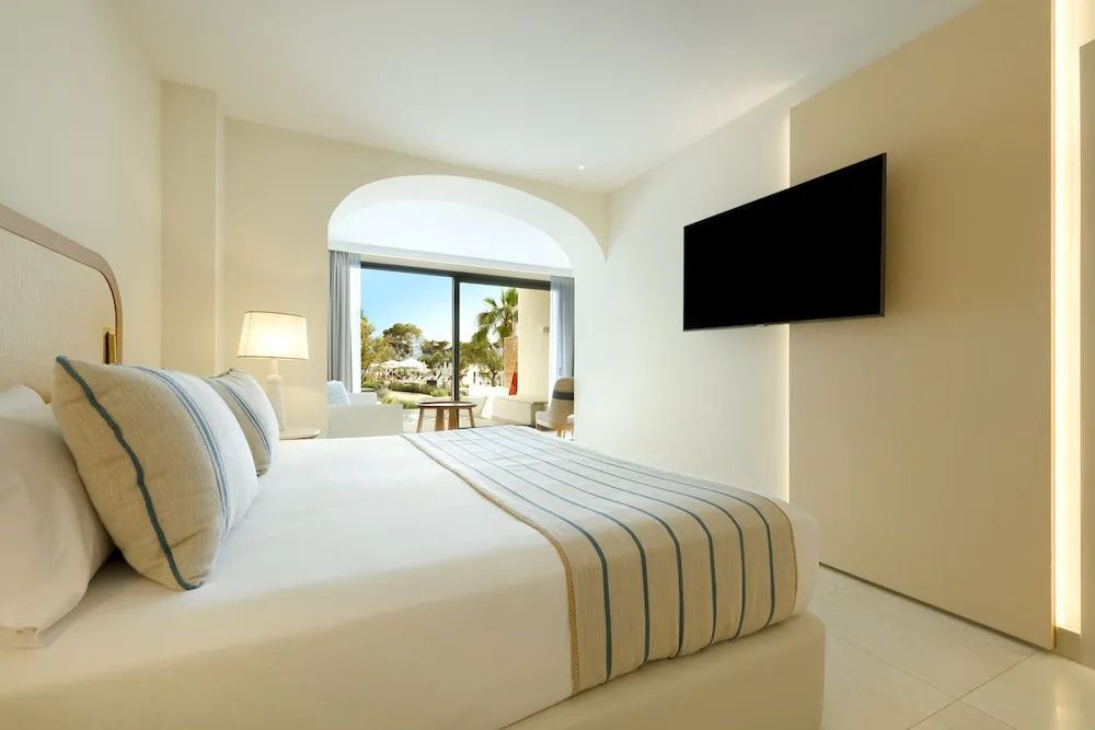 Hell eingerichtetes Hotelzimmer mit Doppelbett, Fernseher und Blick auf den Garten.