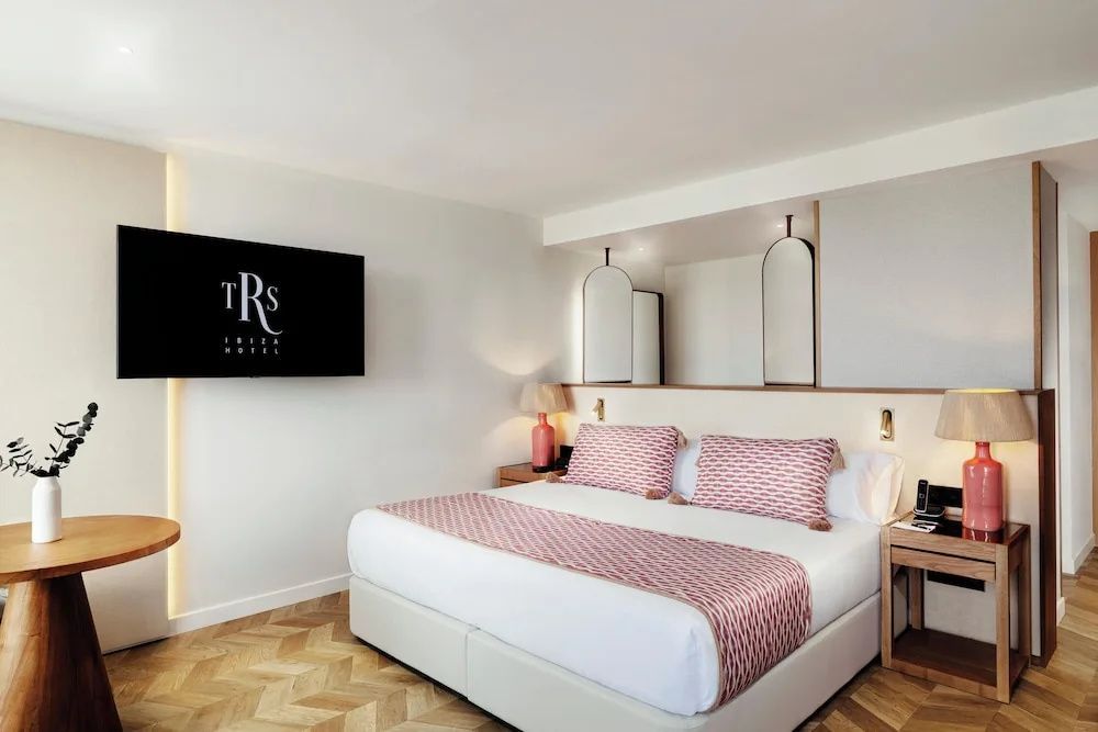 Doppelzimmer mit Parkettboden, rosa gemusterter Bettwäsche und Wandfernseher.