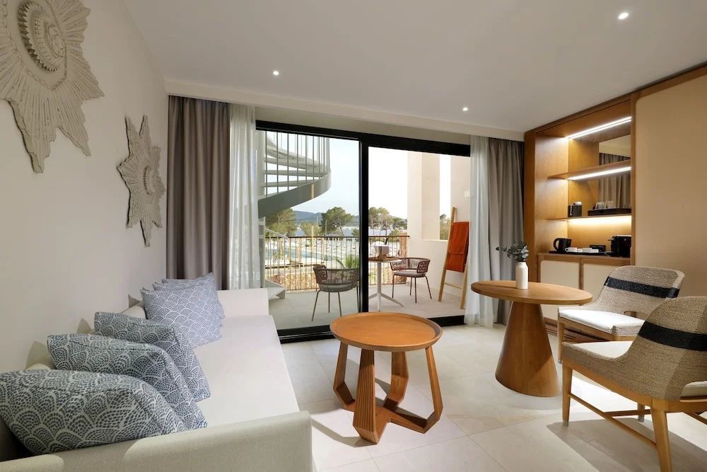 Wohnbereich einer Suite mit hellem Sofa, Holztischen und Zugang zur Terrasse.