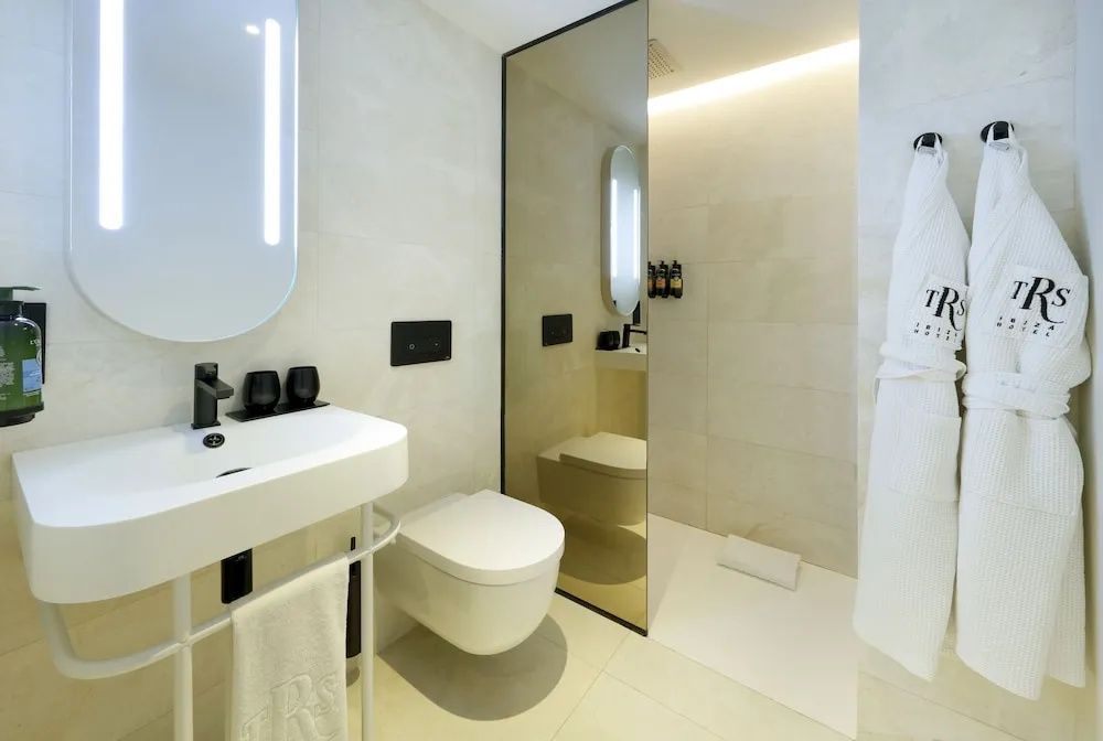 Modernes Badezimmer mit weißem Waschtisch, Toilette und ebenerdiger Dusche hinter Glas.