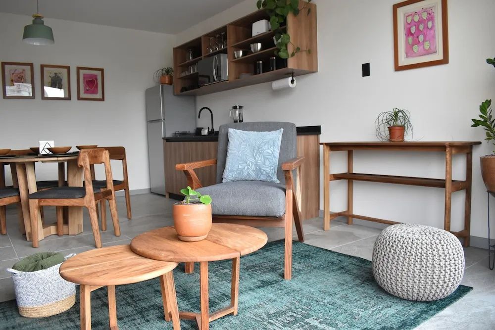 Sitzbereich mit grauem Sessel, blauem Teppich und kleinen Holztischen vor der Küchenzeile.
