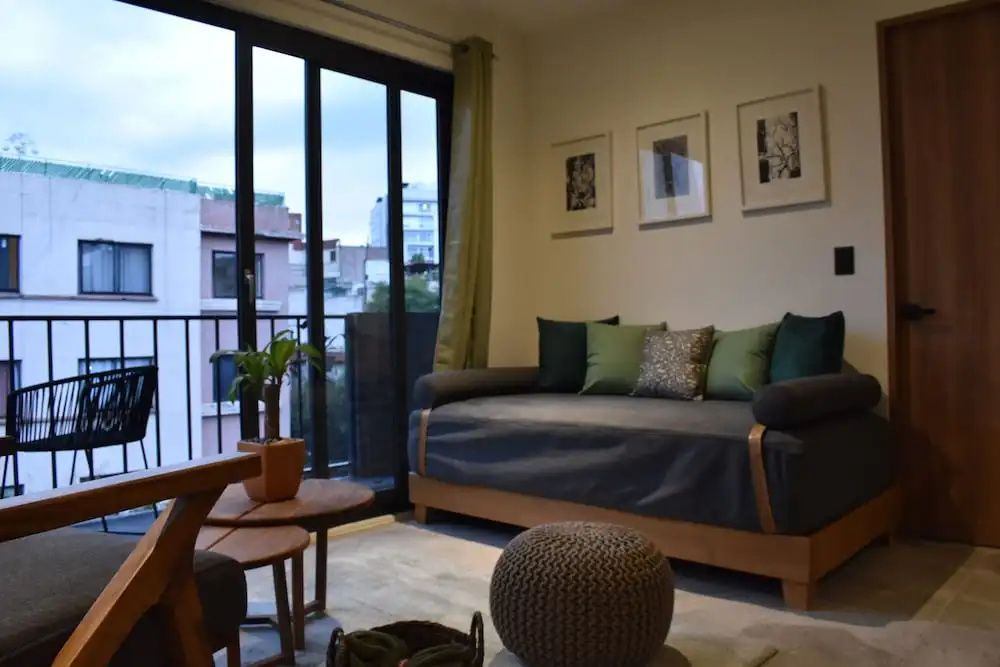 Wohnbereich im Hotelzimmer mit Daybed, grünen Kissen, Wandbildern und Glasbalkontür.