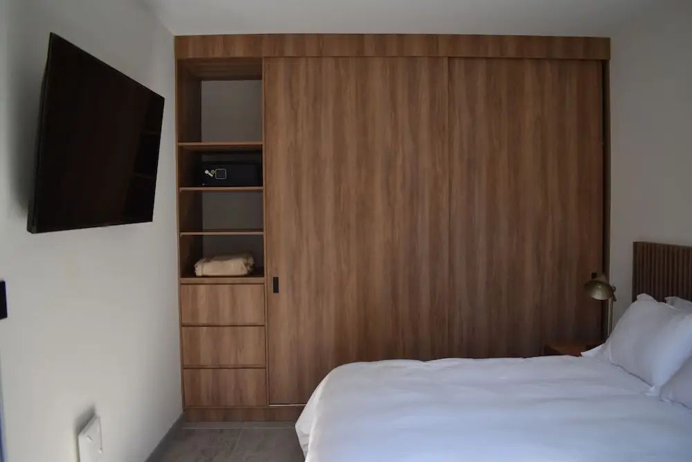 Schlafzimmer mit großem Einbauschrank aus Holz, Safe und Fußende eines Bettes.