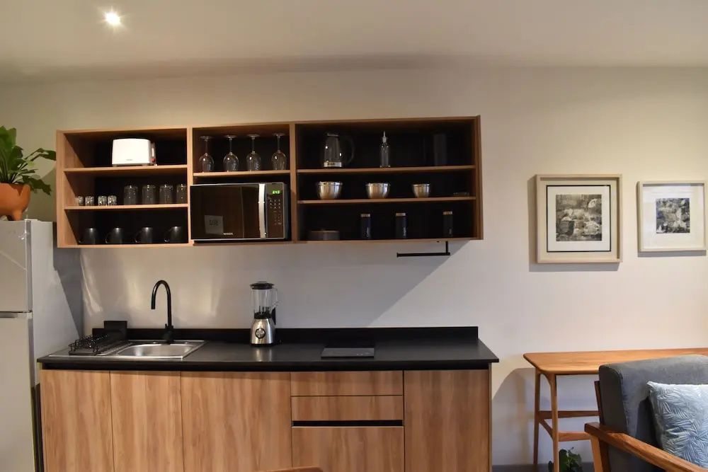 Moderne Küchenzeile aus Holz mit Mikrowelle, Spülbecken und Hängeregalen.