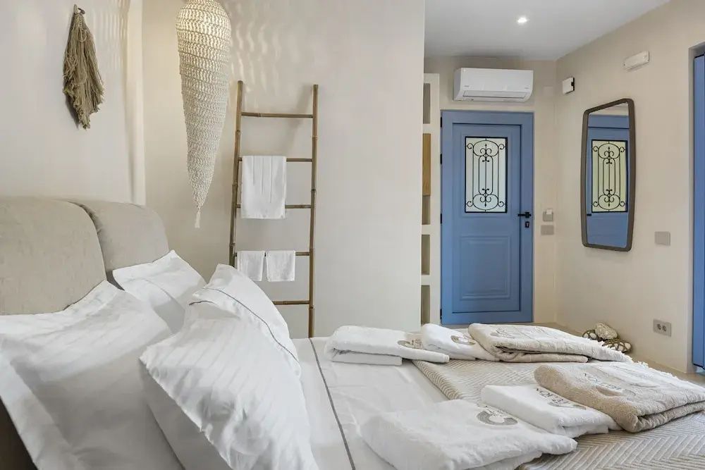 Helles Schlafzimmer mit großem Bett, blauer Eingangstür und Deko Holzleiter.