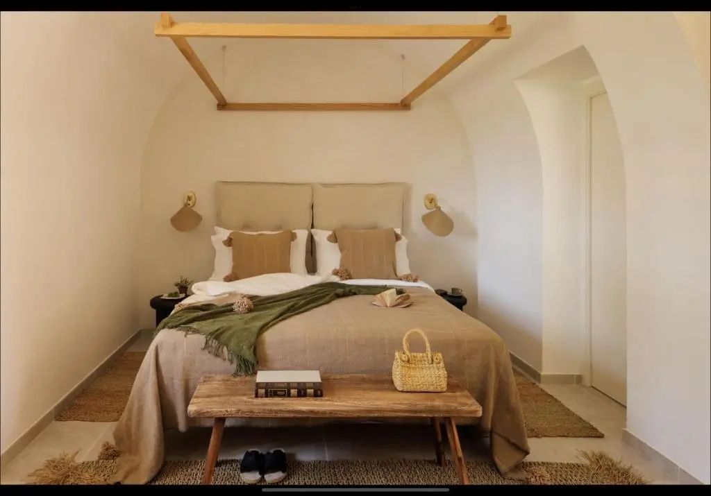 Hell eingerichtetes Schlafzimmer unter einer Gewölbedecke mit Doppelbett und Holzbank.