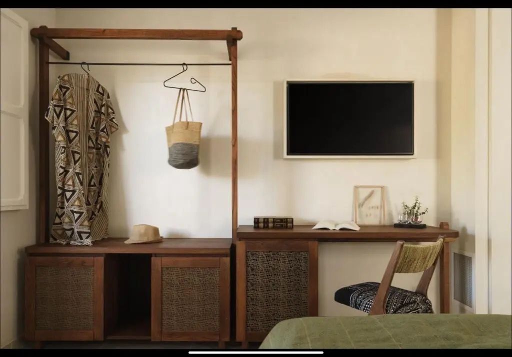 Holzschreibtisch mit Stuhl und offene Garderobe mit Wandfernseher.