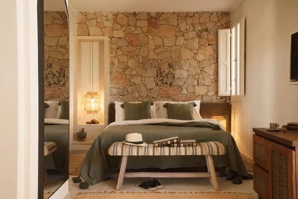 Doppelbett vor einer Natursteinwand mit grüner Bettwäsche und Holzbank.