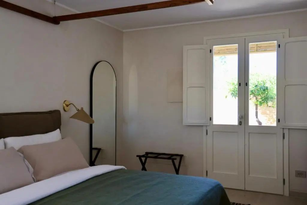 Hell eingerichtetes Hotelzimmer mit Doppelbett, einem Bogen-Ganzkörperspiegel und Balkontür.