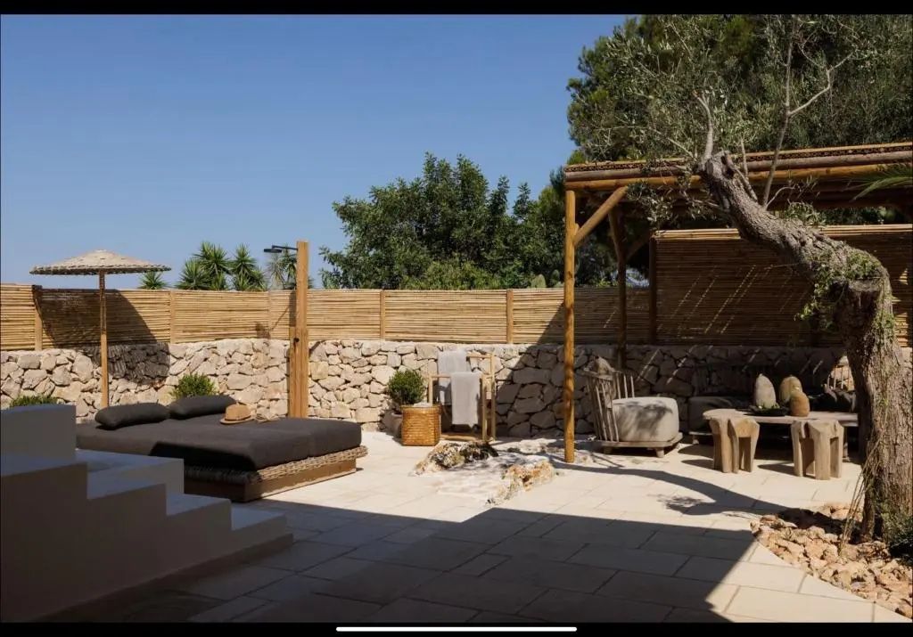 Sonnige Terrasse mit einer breiten Sonnenliege, Natursteinmauer und Holzpergola.