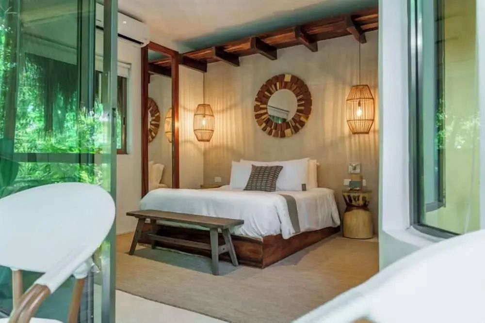 Modernes Hotelzimmer mit Doppelbett, Holzbank, rundem Wandspiegel und Flechtlampen.