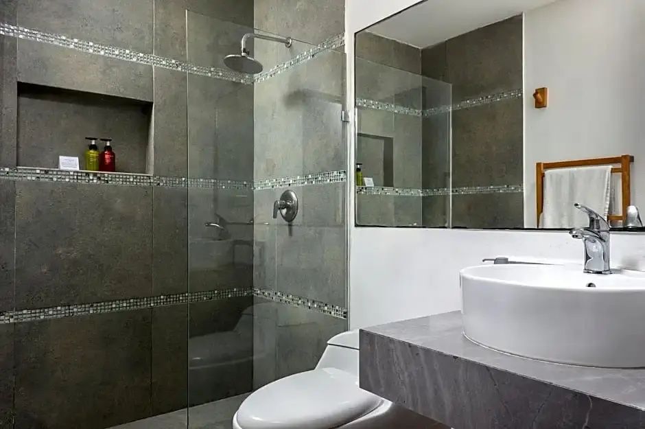 Badezimmer mit dunklen Fliesen, einer begehbaren Glasdusche und einem Waschbecken.