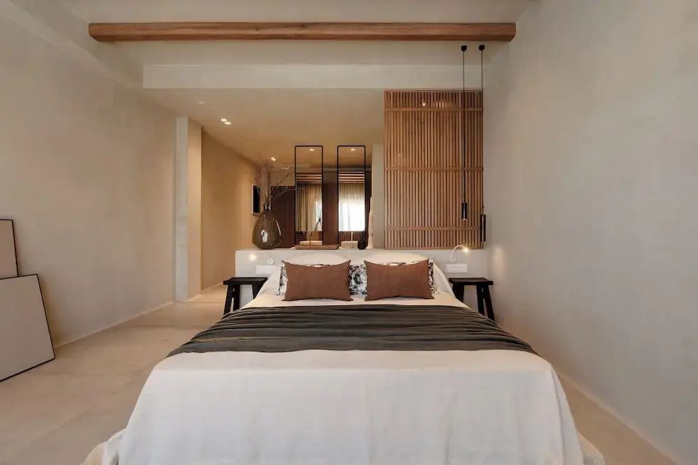 Frontale Ansicht eines Doppelbetts in hellem Zimmer mit Holzdecke und offenem Bad im Hintergrund.