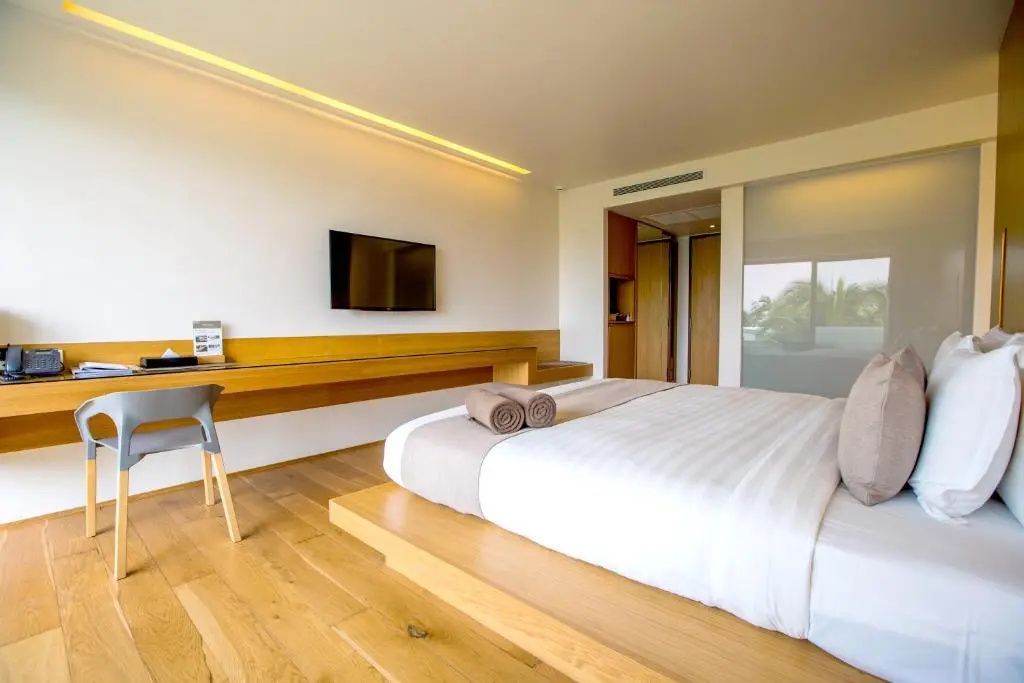 Helles Hotelzimmer mit Doppelbett auf Holzpodest, Fernseher an der Wand und Schreibtisch.