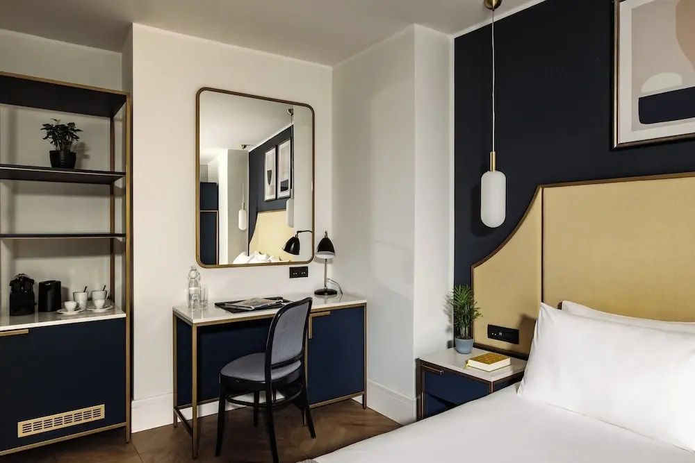 Modernes Hotelzimmer mit Schreibtisch, Wandspiegel und gelbem Kopfteil am Bett.