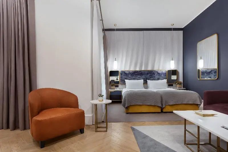 Ein eingerichtetes Hotelzimmer mit Doppelbett, gelbem Untergestell und Sessel.