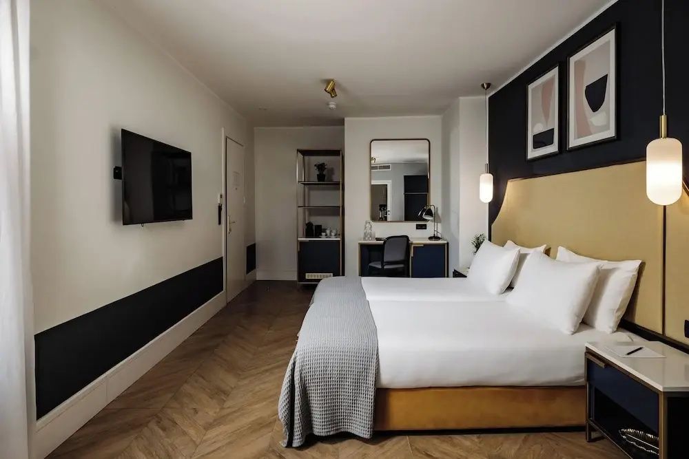 Modernes Hotelzimmer mit Doppelbett, Parkettboden, Fernseher an der Wand und Schreibtisch.