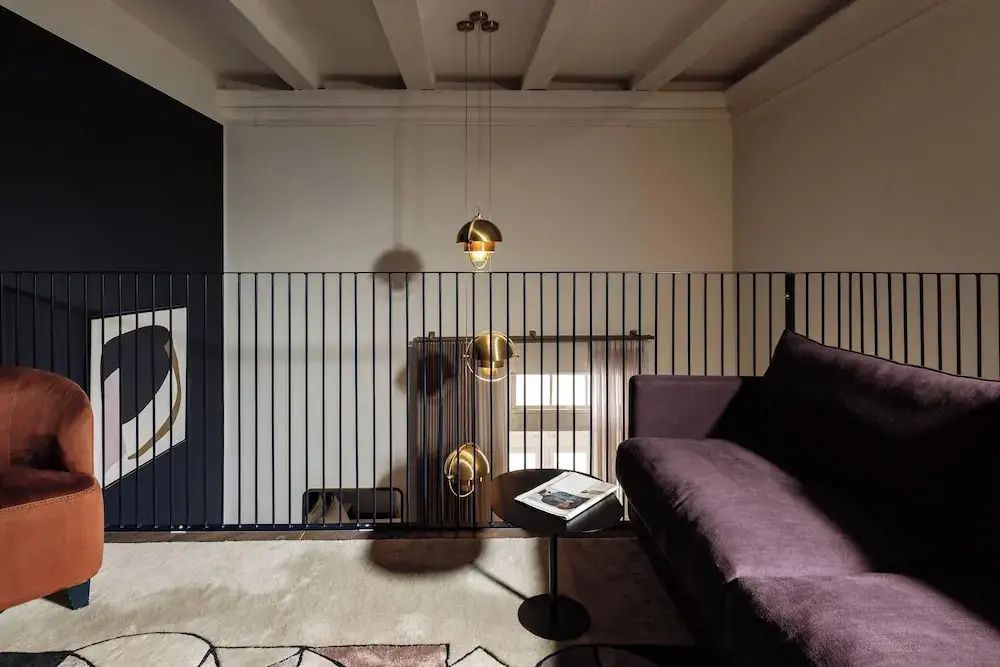 Sitzbereich auf einer Empore mit dunklem Sofa, Teppich und einer Hängelampe aus Messing.