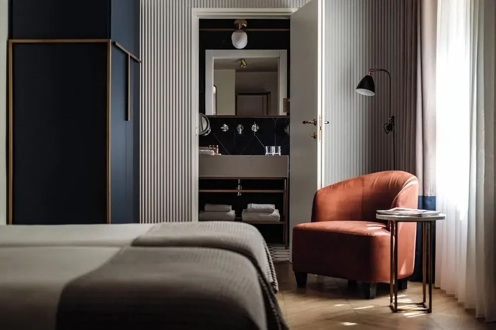 Hotelzimmer mit Doppelbett im Vordergrund, Sessel und Blick ins angrenzende Bad.