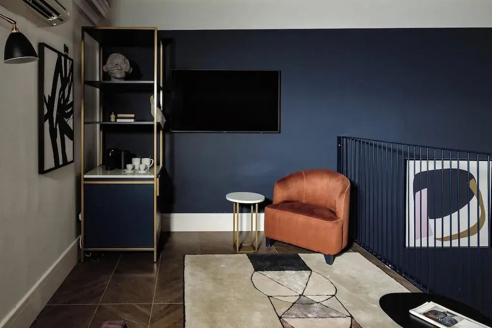 Sitzbereich im Zimmer mit einem Samtsessel in Terracotta, Wandfernseher und dunkler Wand.