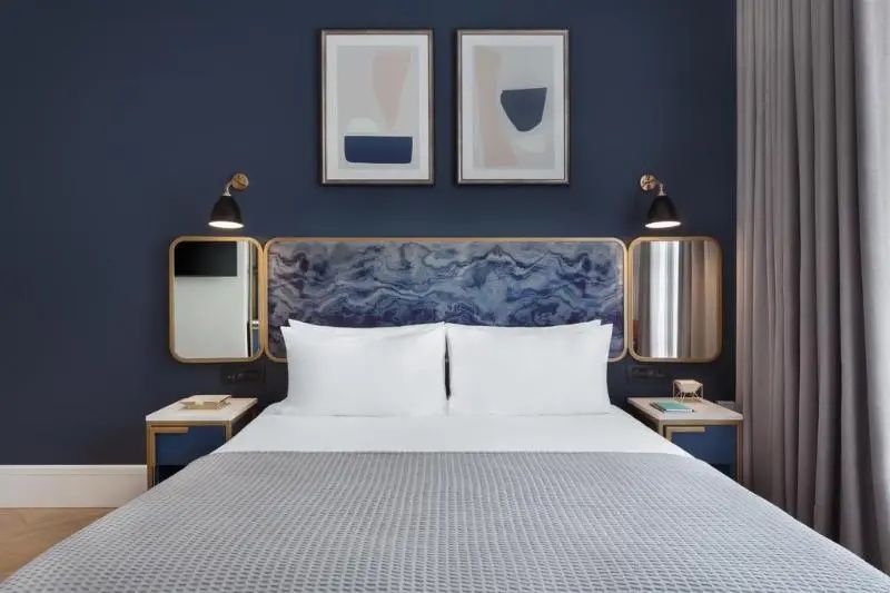 Blick auf ein Doppelbett mit weißer Bettwäsche, dunkelblauer Wand und zwei Kunstdrucken