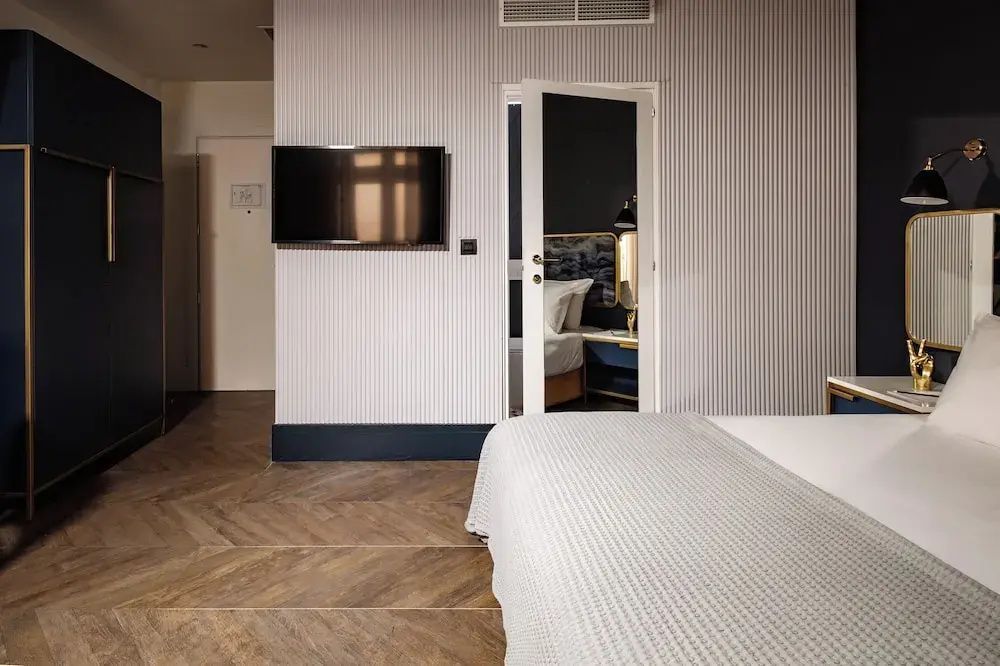 Blick durch das Hotelzimmer mit Wandfernseher auf eine geöffnete Tür zum Schlafbereich.