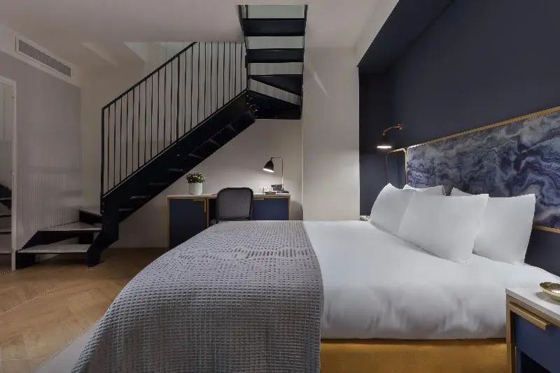 Doppelbett in einem Hotelzimmer mit dunkler Wand und Treppe zum Obergeschoss.