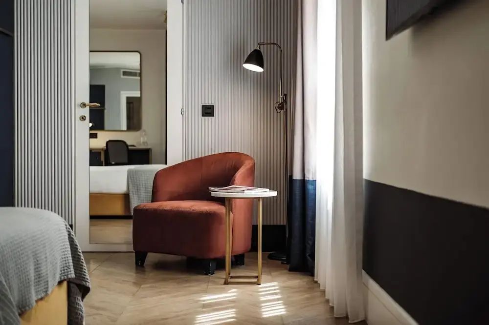 Sitzecke im Hotelzimmer mit rotem Polstersessel, Beistelltisch und Stehlampe am Fenster.