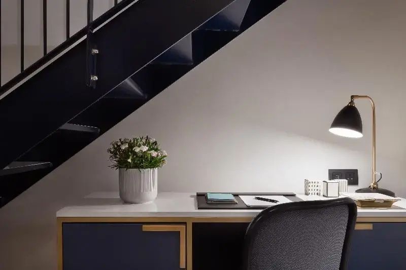 Schreibtisch mit Pflanze und Lampe unter einer modernen Metalltreppe.