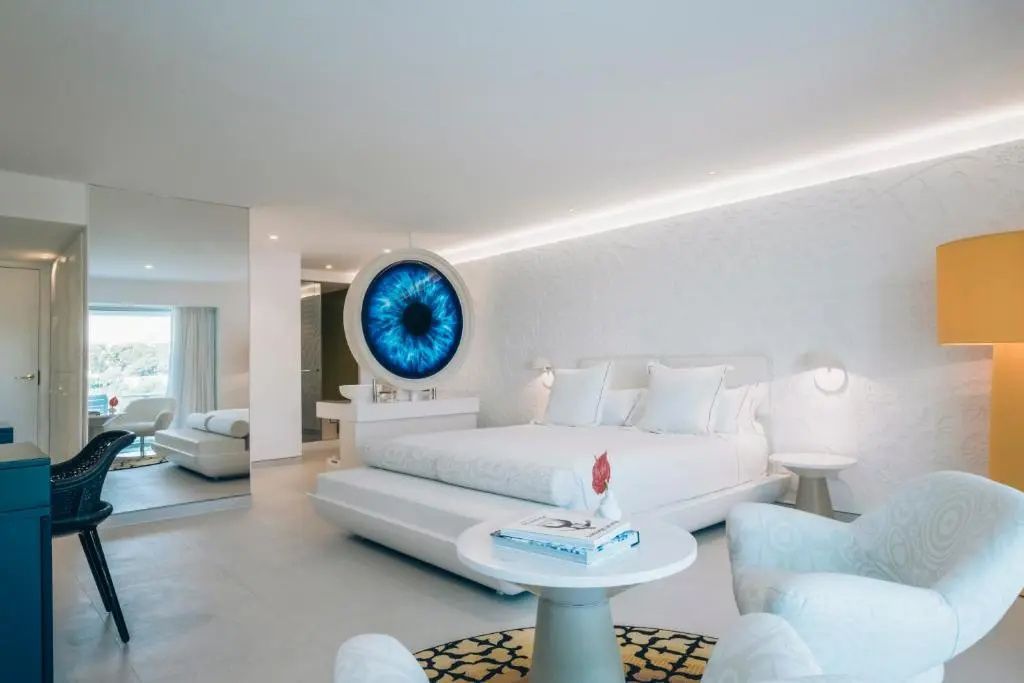 Modernes weißes Hotelzimmer mit großem Doppelbett und blauem Kunstwerk an der Wand.