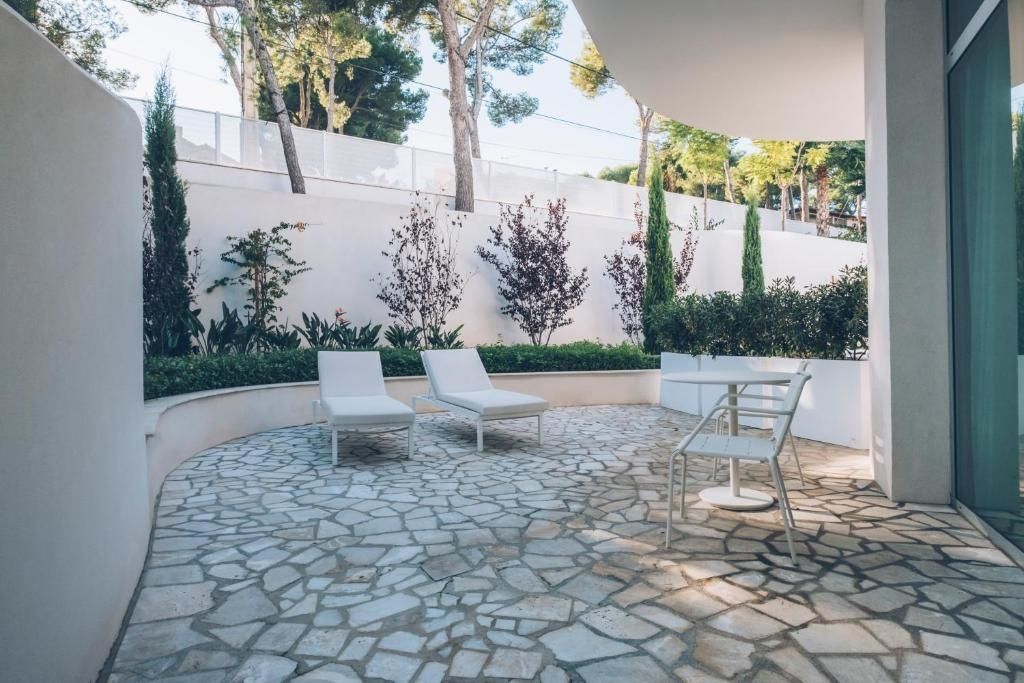 Sonnige Terrasse mit Natursteinpflaster, zwei Sonnenliegen, Tisch, Stühlen und grünen Pflanzen.