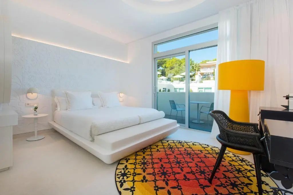 Weißes Hotelzimmer mit buntem Teppich und Zugang zum möblierten Balkon