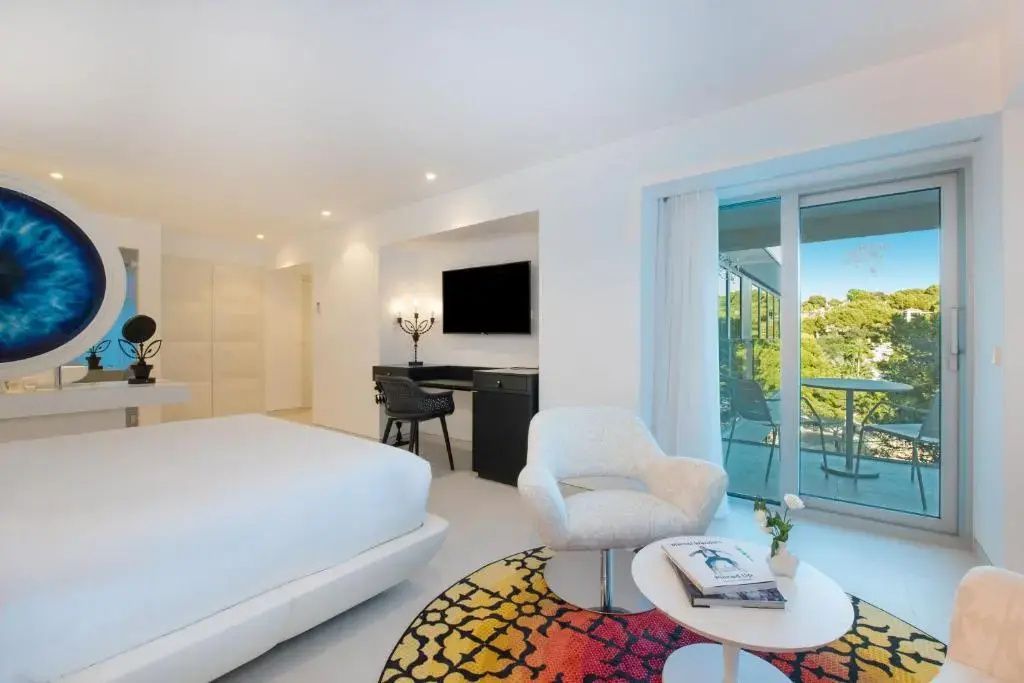 Sitzbereich im Hotelzimmer mit weißem Sessel, Couchtisch und Zugang zum Balkon