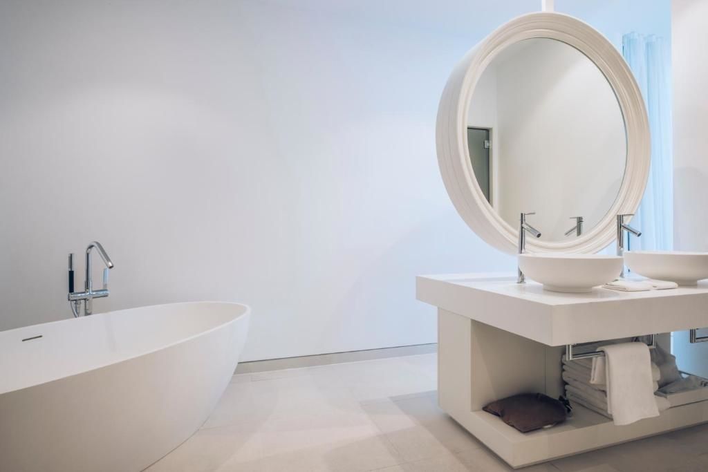 Weißes Badezimmer mit freistehender Badewanne und rundem Spiegel am Waschtisch.